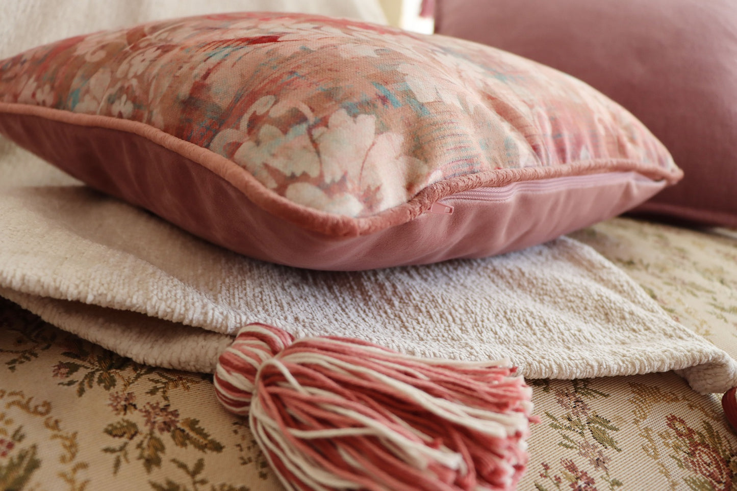 floral cushion cover with piped edge on a textured surface with a tassel.