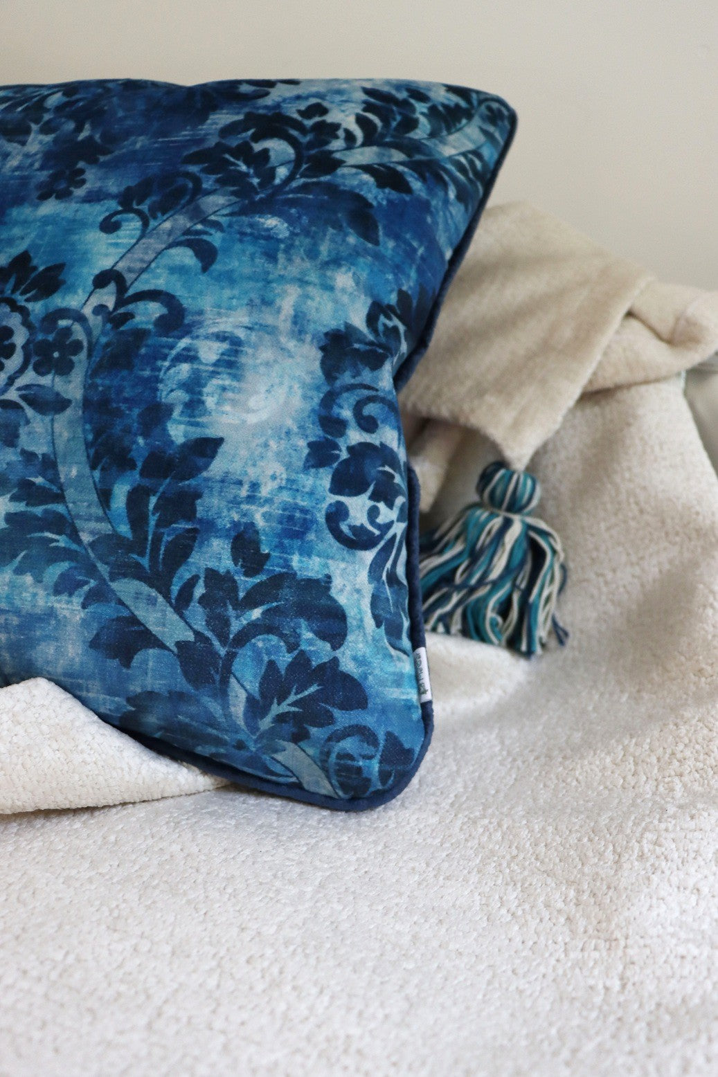 Blue floral cushion cover with piped edge on a white blanket