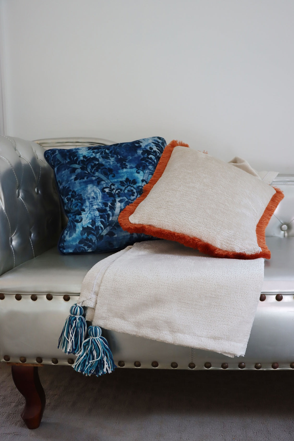 Decorative orange and blue floral cushion cover with piped edge and blanket on a gray sofa against a white wall