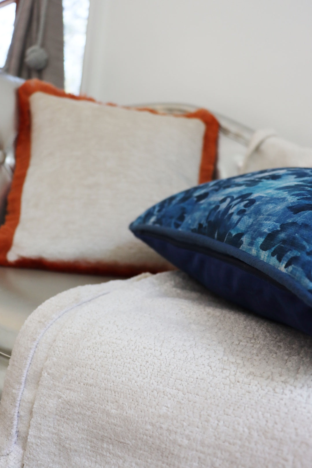Close-up of a sofa with decorative pillows including a blue floral cushion cover with piped edge and an orange-trimmed white one.