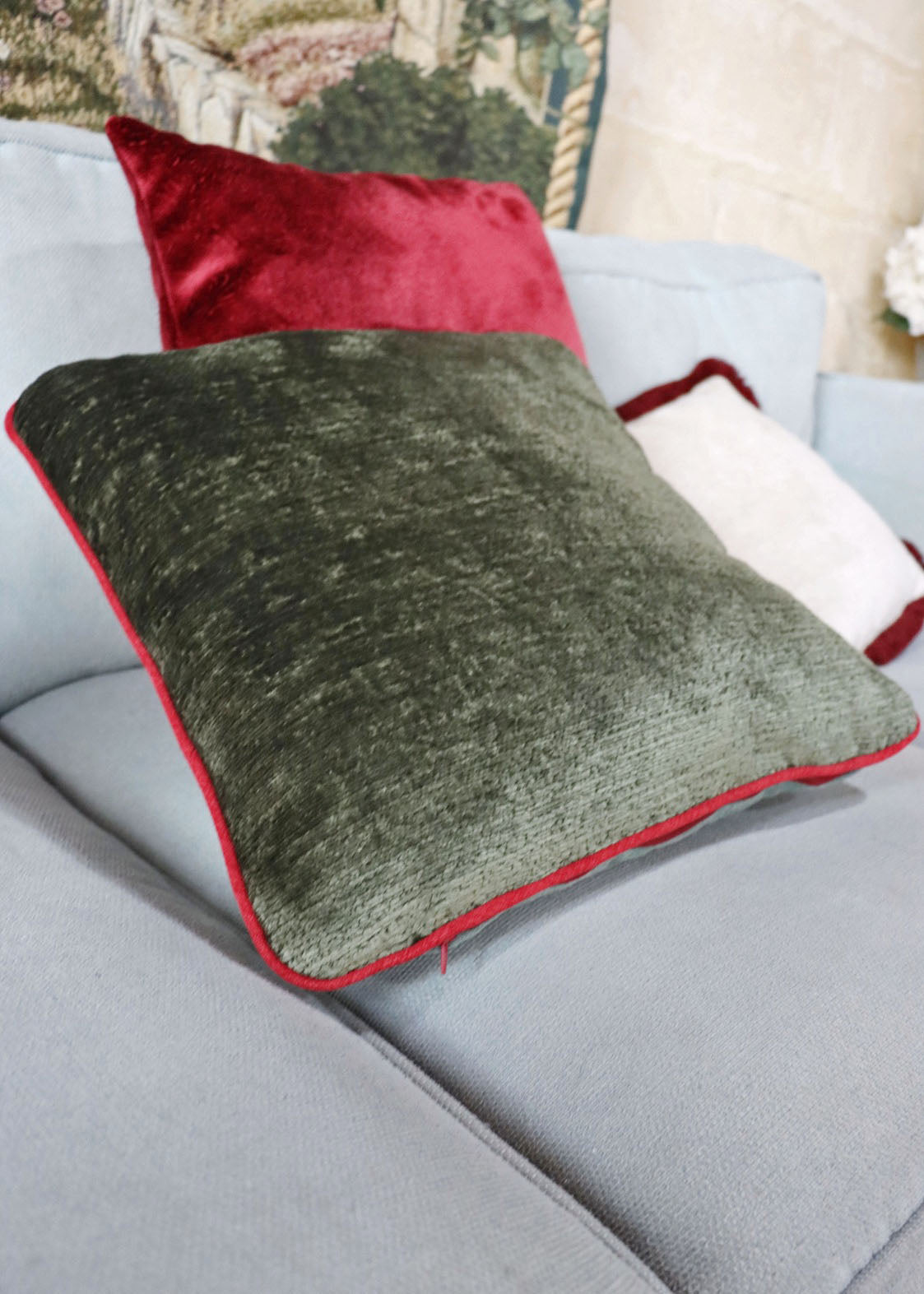 Green chenille cushion cover with contrasting piping on a sofa with a blurred background