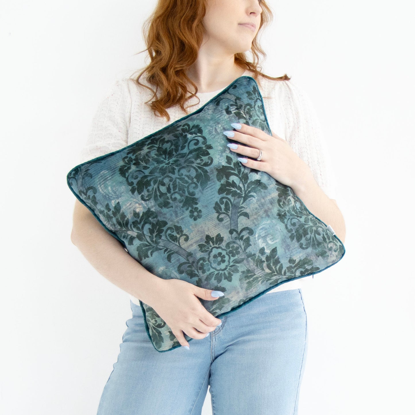 Woman holding a blue floral cushion cover with piped edge on a white background