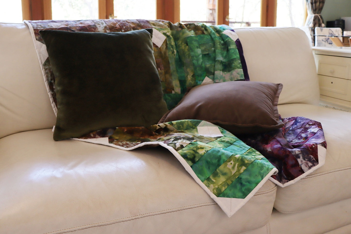 Colorful quilt and textured velvet cushion cover on a beige sofa with a neutral background