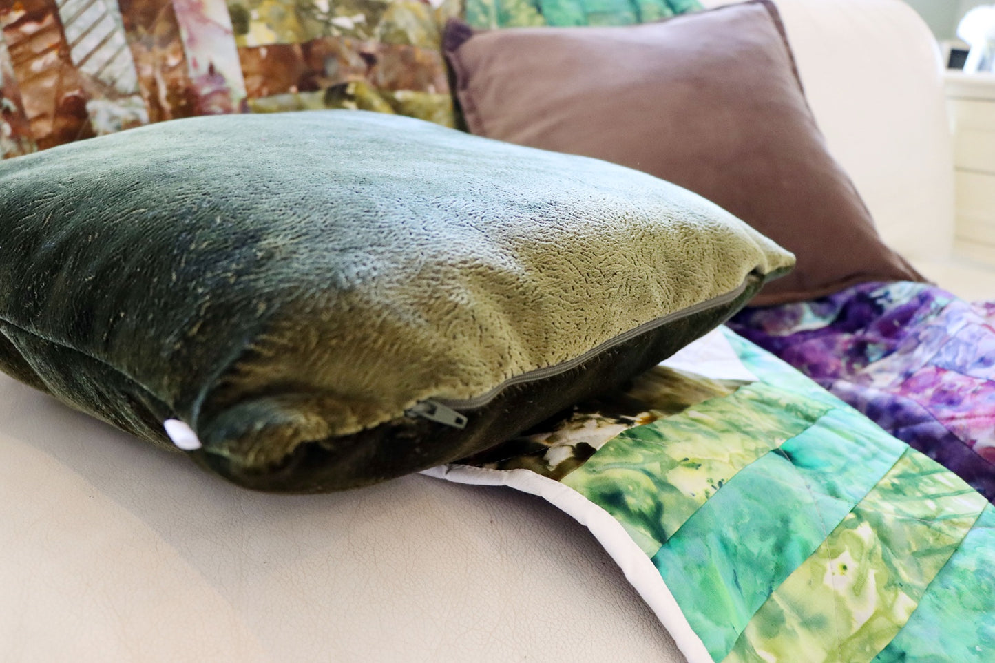 Green textured velvet cushion cover on a couch with a colorful quilt and brown pillow in the background