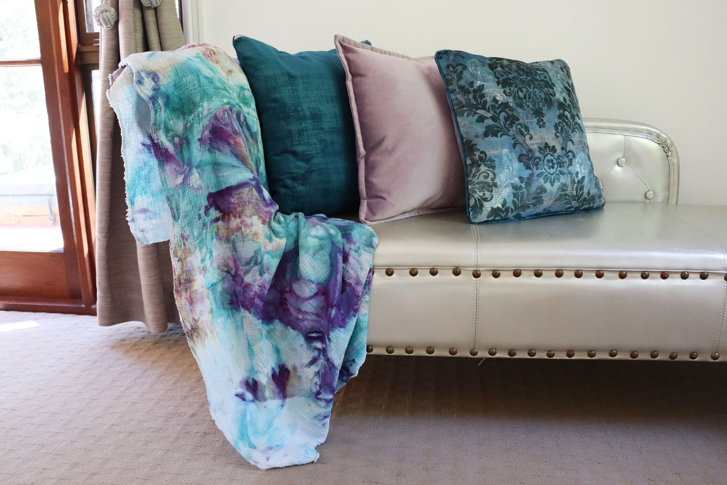 Colorful blanket and teal flora cushion cover with piped edge on a white sofa in a room with a window.