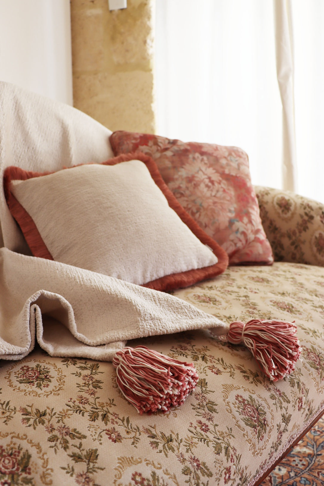 Floral-patterned sofa with floral cushion cover with piped edge and a blanket featuring tassels.