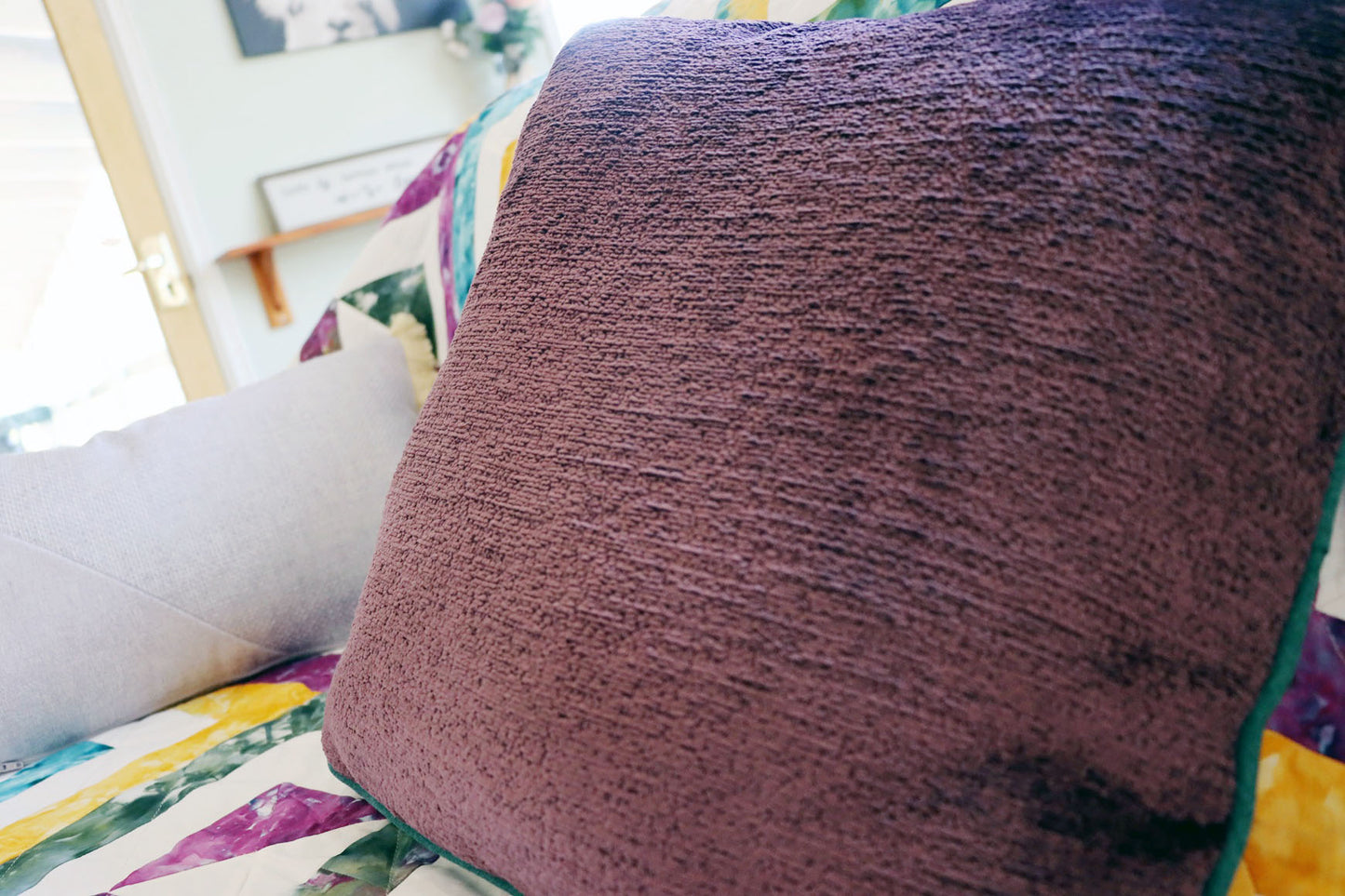 Close-up of a textured purple chenille cushion cover with contrasting piping on a colourful fabric surface.