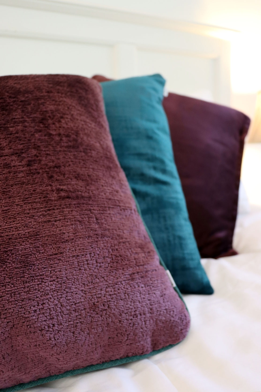 Purple chenille cushion cover with contrasting piping on a bed.