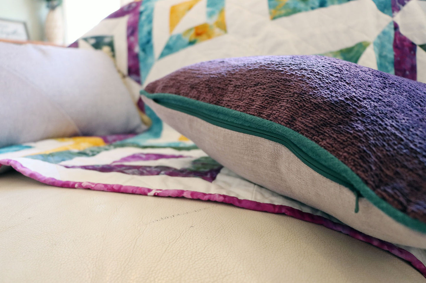 Colourful quilt with textured chenille cushion cover with contrasting piping on a sofa