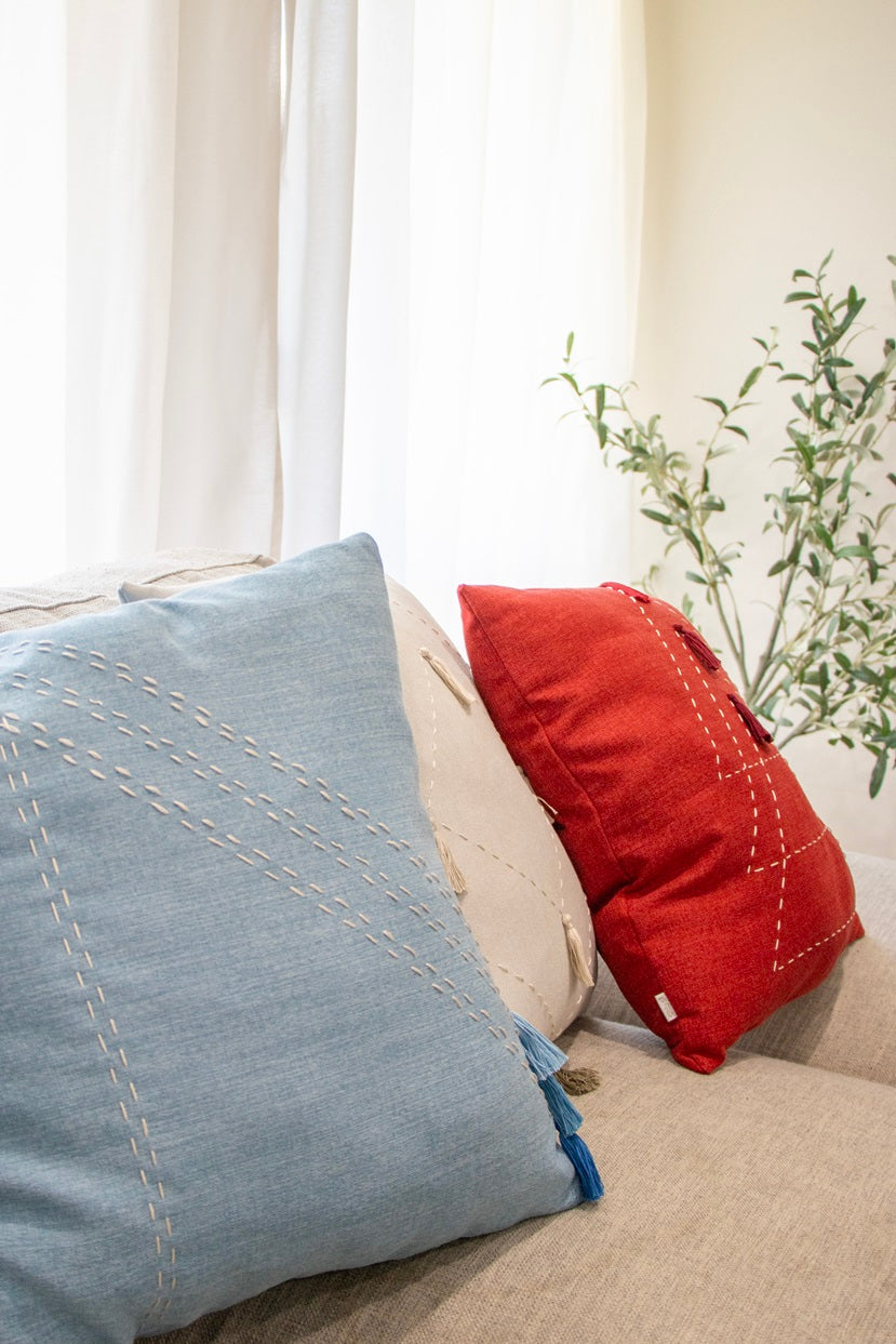 Red, blue and white cushion cover with embroidery and tassels on sofa