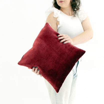 Person holding a red textured velvet cushion cover against a white background
