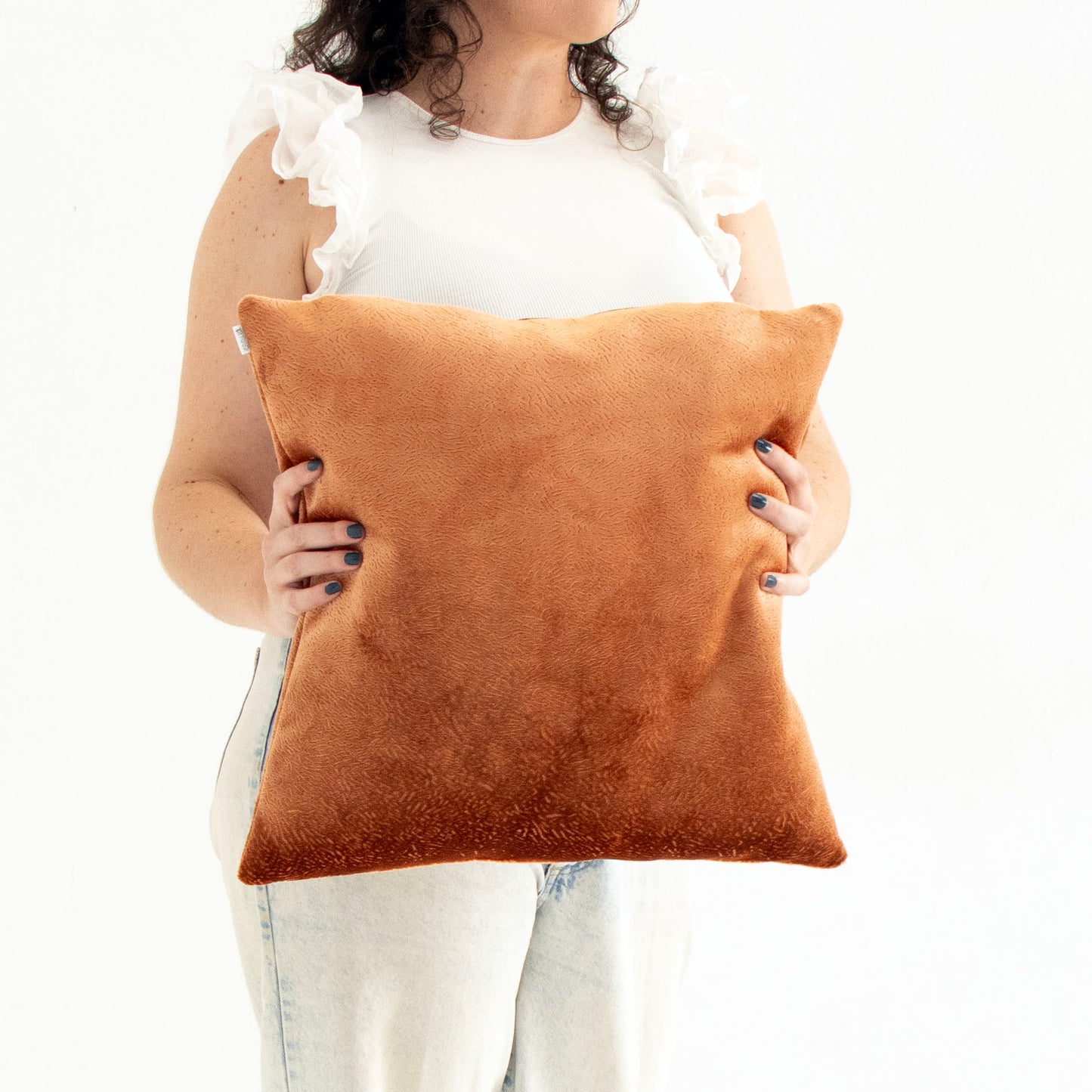 Person holding a brown textured velvet cushion cover against a white background