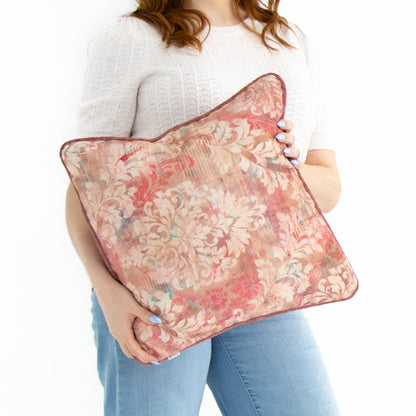 Person holding a floral cushion cover with piped edge against a white background