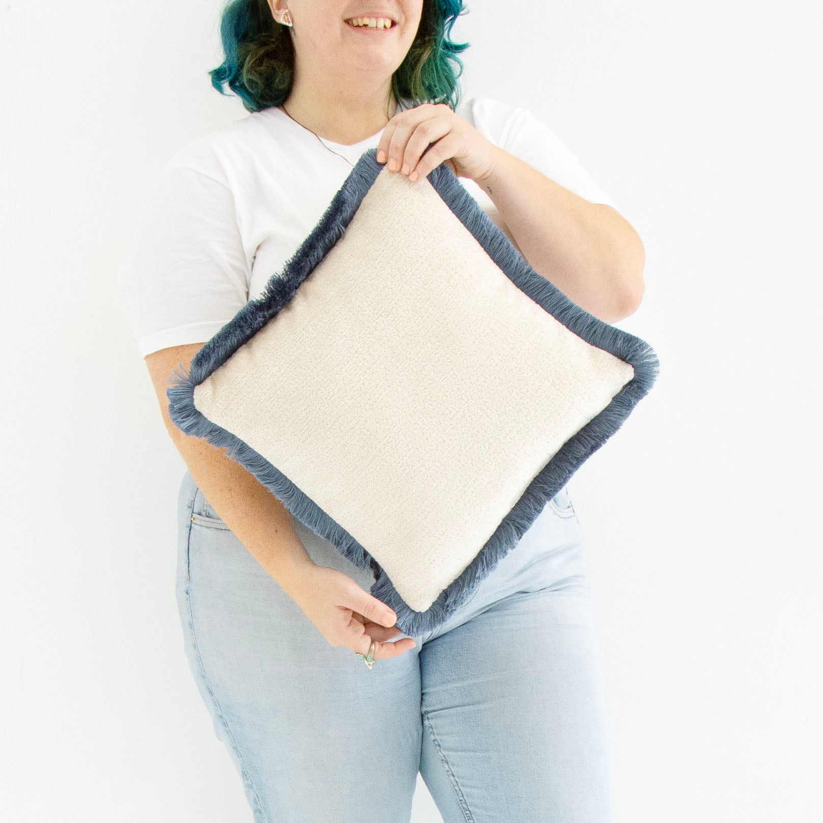 Person holding a blue chenille cushion cover with cotton fringe against a white background