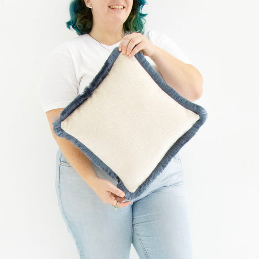 Person holding a blue chenille cushion cover with cotton fringe against a white background