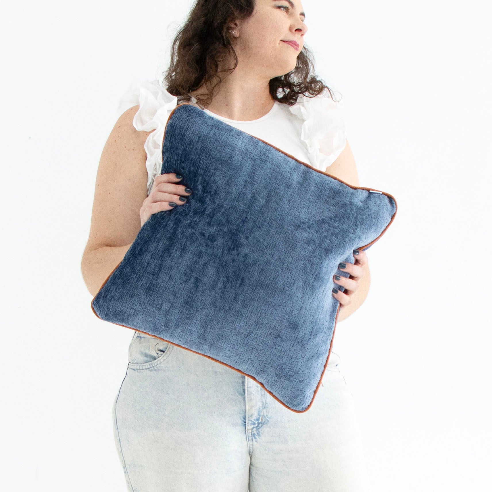Woman holding a blue chenille cushion cover with contrasting piping against a white background