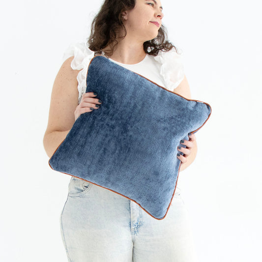Woman holding a blue chenille cushion cover with contrasting piping against a white background