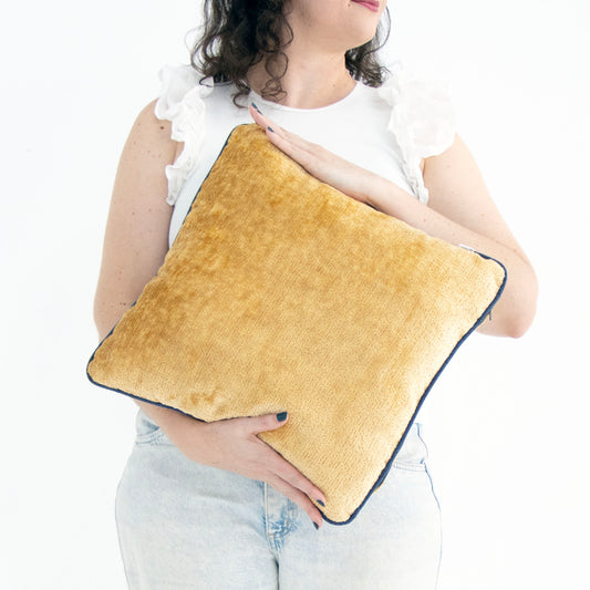 Person holding a yellow chenille cushion cover with contrasting piping with a white background