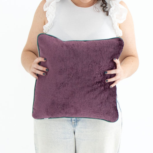 Person holding a purple chenille cushion cover with contrasting piping with a white background