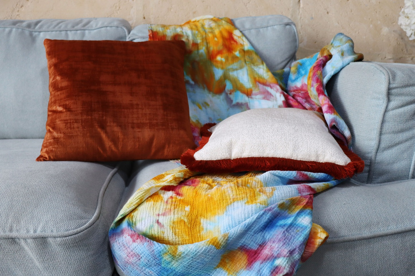 Gray sofa with colourful throw and orange chenille cushion cover with cotton fringe on a textured wall background