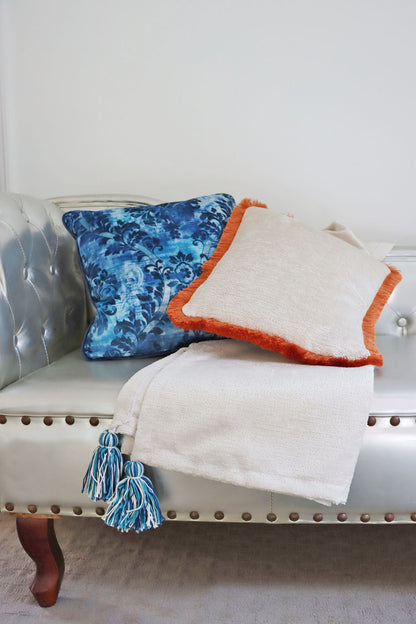 Decorative orange chenille cushion cover with cotton fringe and blanket on a white couch with a neutral background