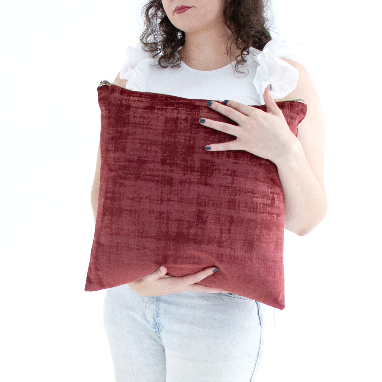 Person holding a maroon handmade textured velvet cushion cover with exposed zipper against a white background