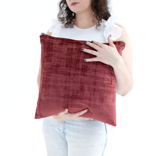 Person holding a maroon handmade textured velvet cushion cover with exposed zipper against a white background