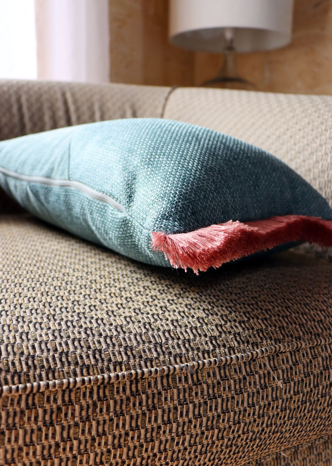 Textured oblong cushion cover with cotton fringe on a brown sofa with a blurred background