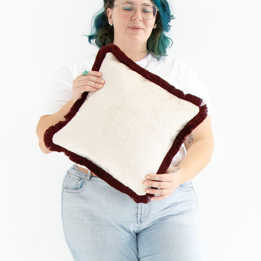 Person holding a red chenille cushion cover with cotton fringe