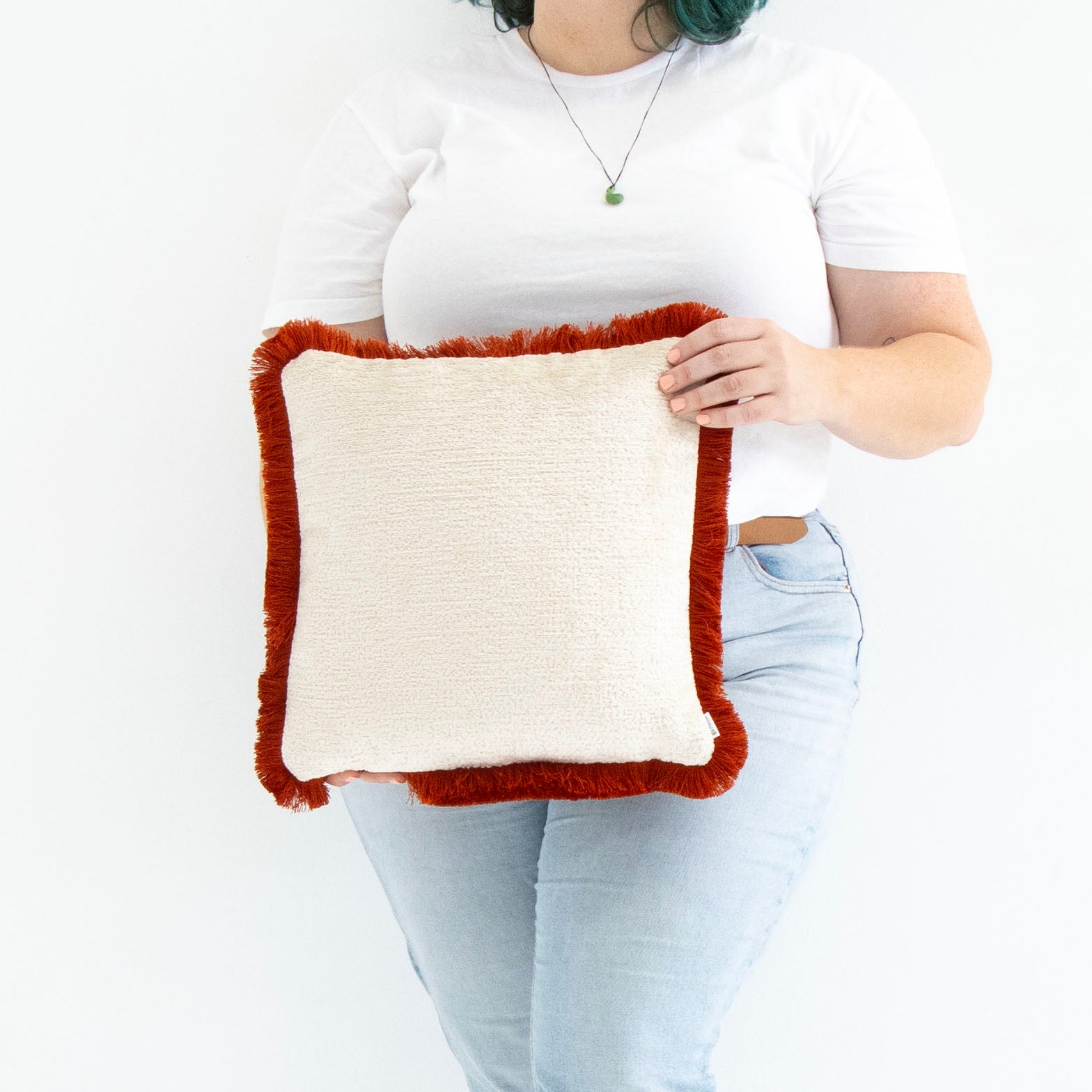 Person holding a chenille cushion cover with cotton fringe against a white background