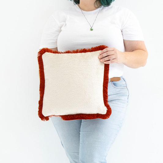 Person holding a chenille cushion cover with cotton fringe against a white background