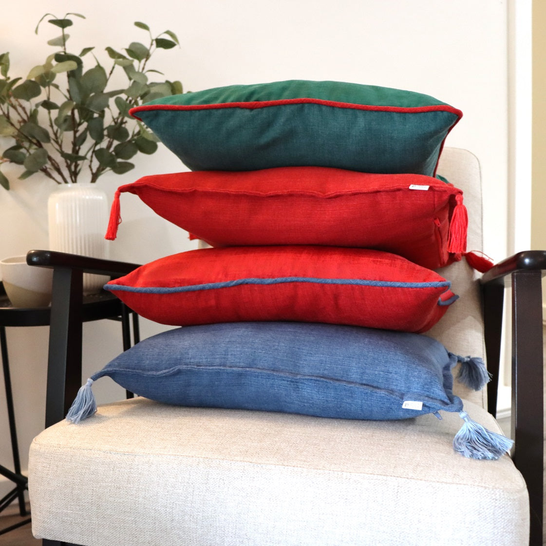 Stack of green, red and blue Velvet Cushion Cover with Contrasting Piping on chair