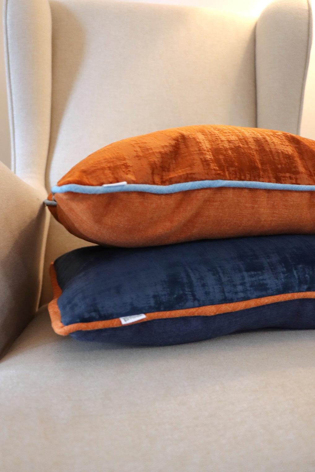 Stack of orange and blue Velvet Cushion Cover with Contrasting Piping on chair