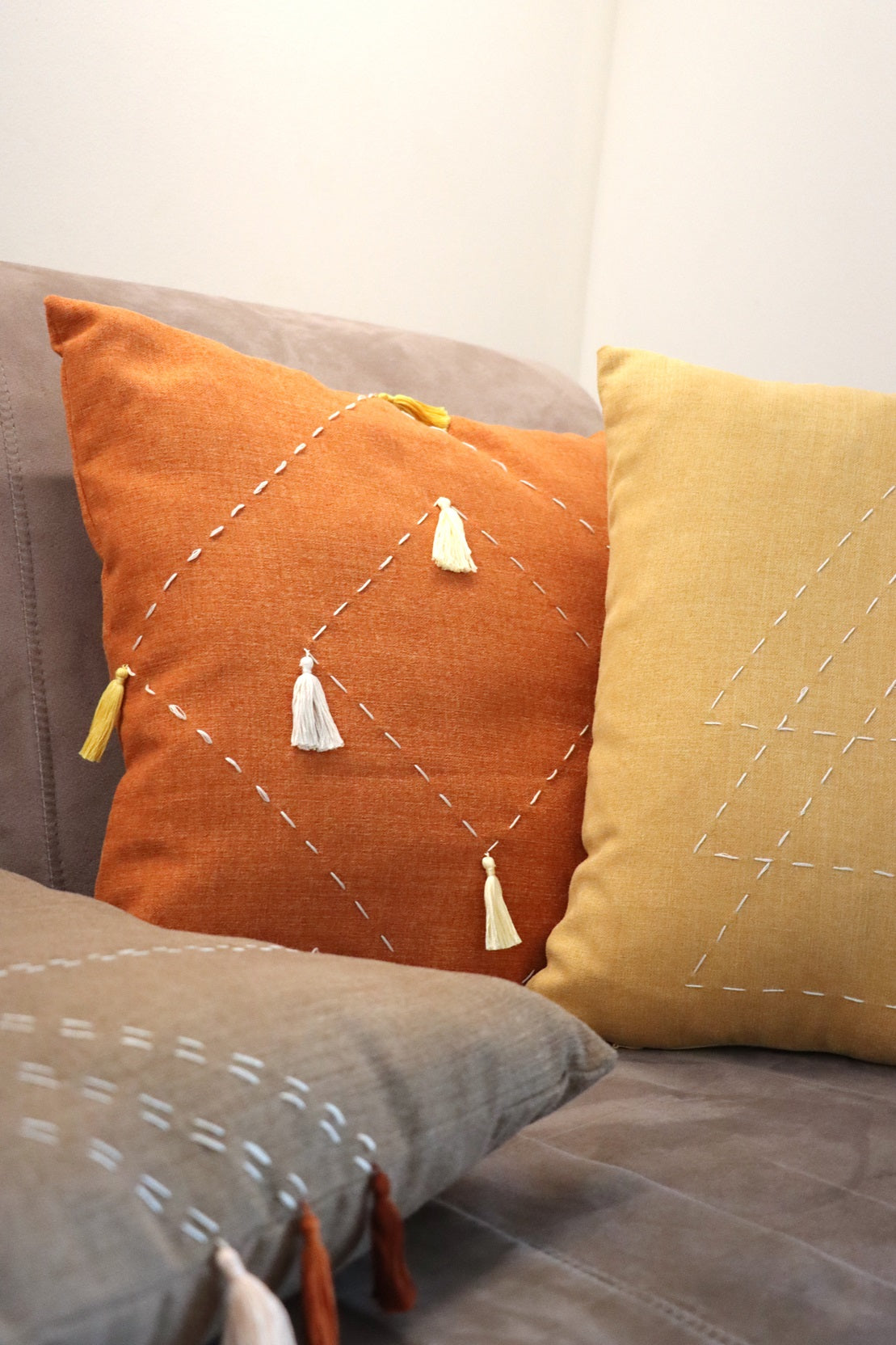 Brown, orange and yellow cushion cover with embroidery and tassels on couch