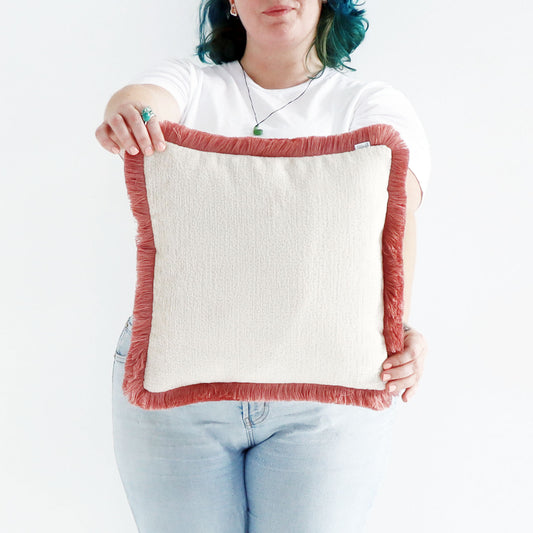 Person holding a square chenille cushion cover with cotton fringe against a white background