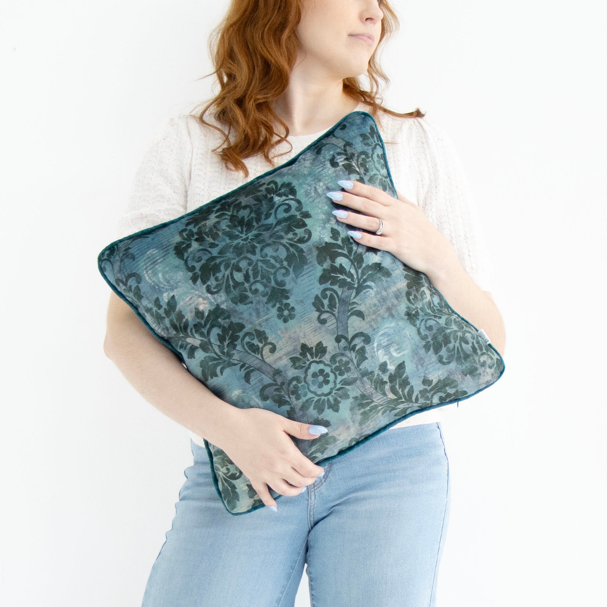 Woman holding a blue floral cushion cover with piped edge on a white background