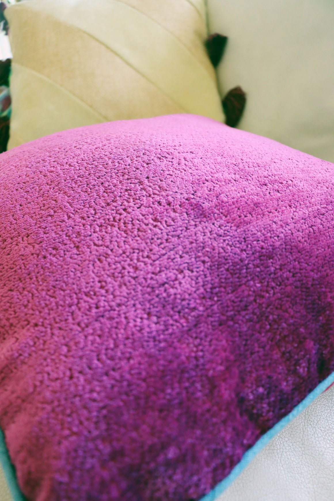 Close-up of a textured pink chenille cushion cover with contrasting piping on a light-colored couch.