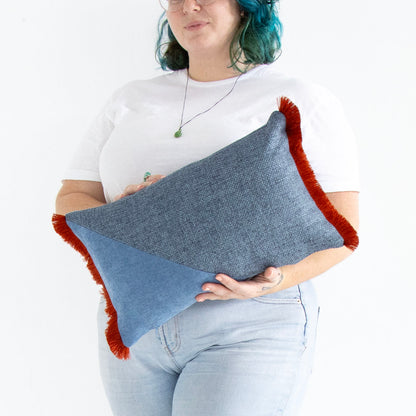 Person holding a blue oblong cushion cover with cotton fringe against a white background