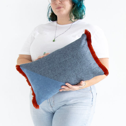 Person holding a blue oblong cushion cover with cotton fringe against a white background