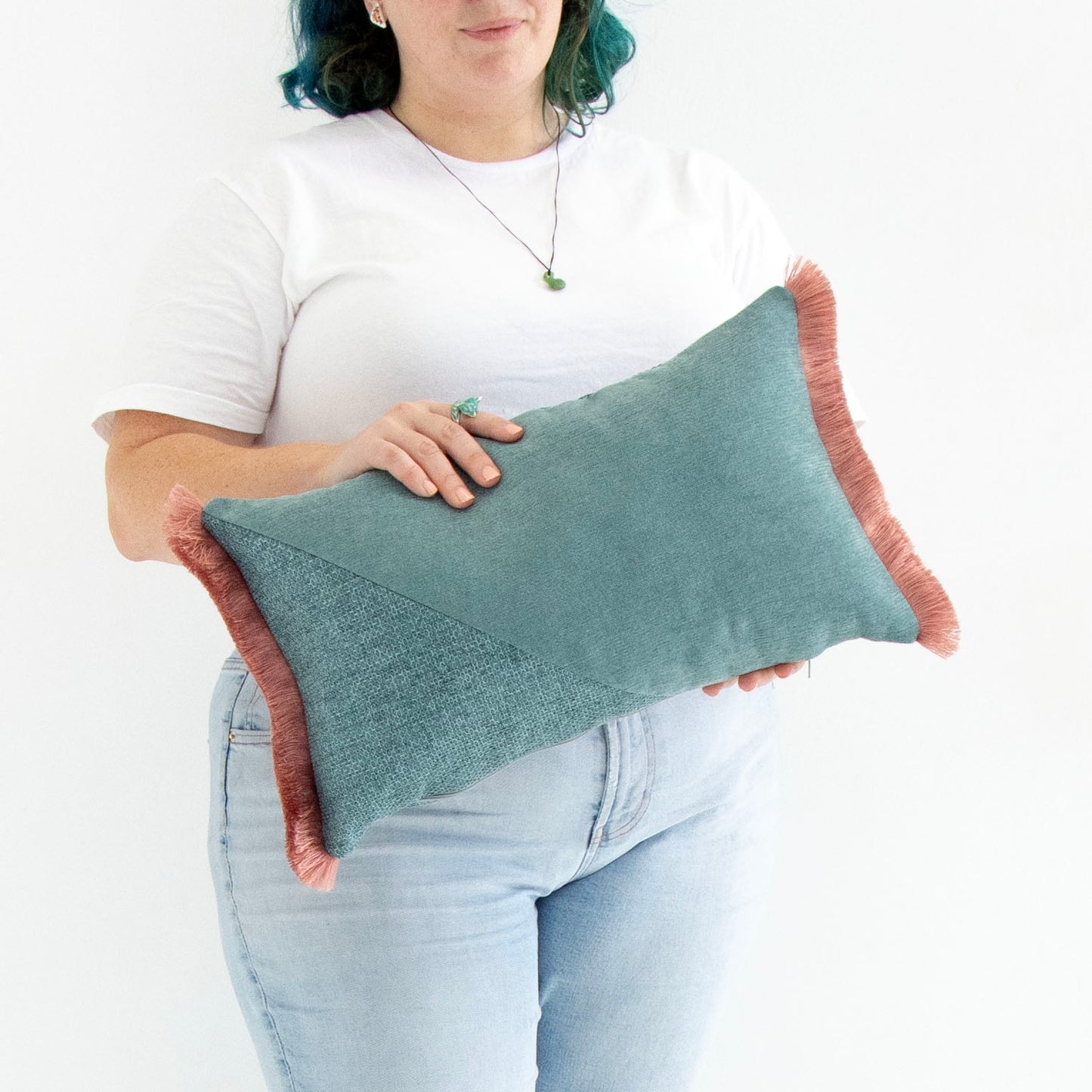 Person holding a teal oblong cushion cover with cotton fringe against a white background