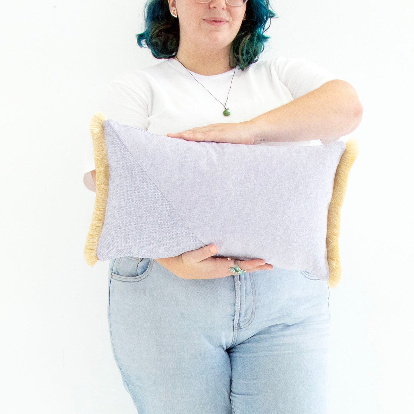 Person holding a light purple oblong cushion cover with cotton fringe against a white background