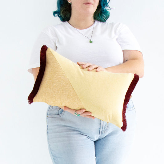 Person holding a yellow and red oblong cushion cover with cotton fringe against a white background