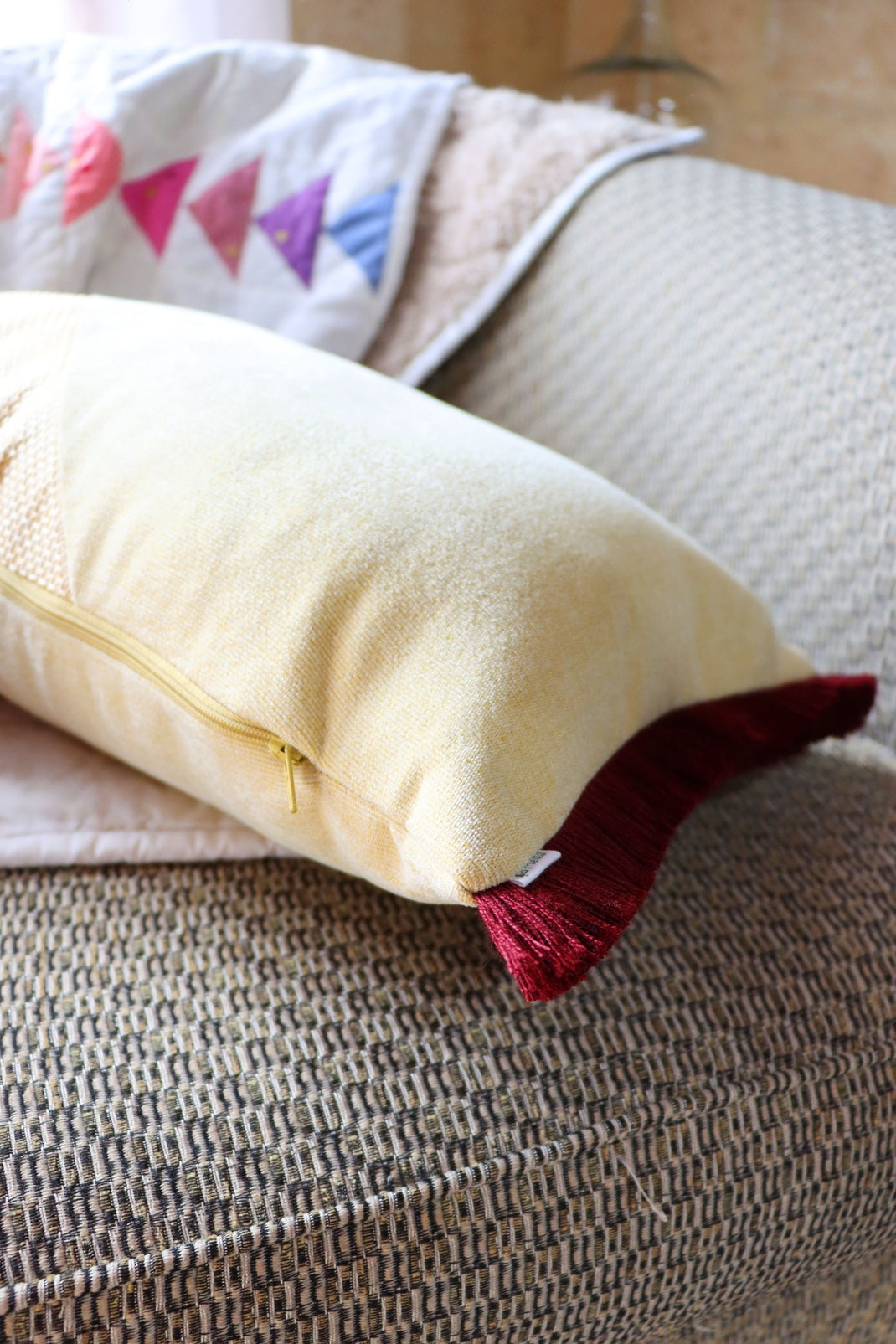 Close-up of a yellow and red oblong cushion cover with cotton fringe zipper on a textured surface.