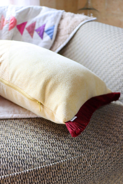 Close-up of a yellow and red oblong cushion cover with cotton fringe zipper on a textured surface.