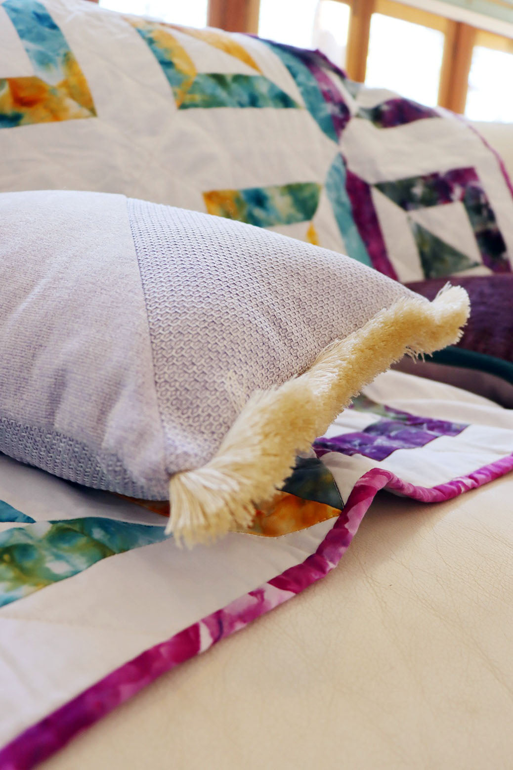 Colourful quilt with a textured oblong cushion cover with cotton fringe on a bed