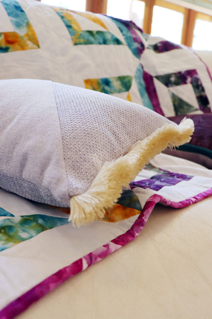 Colourful quilt with a textured oblong cushion cover with cotton fringe on a bed