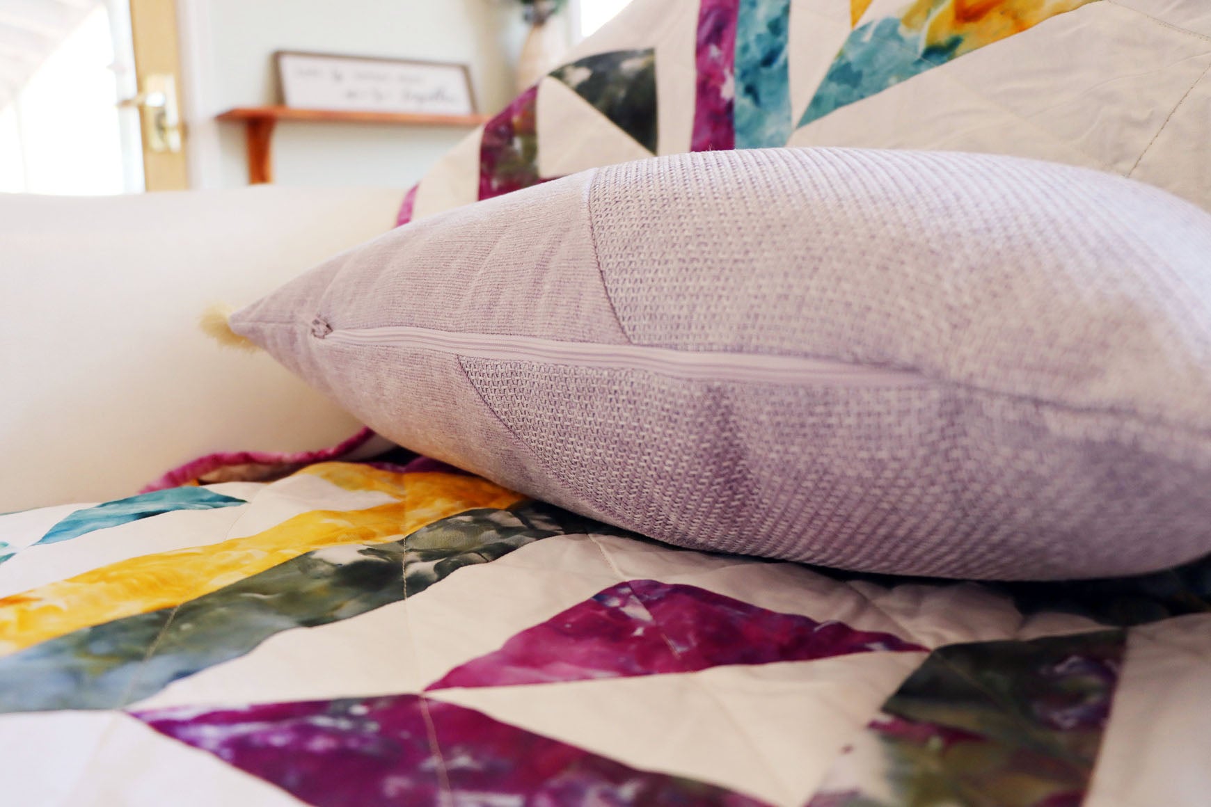 Close-up of a textured oblong cushion cover with cotton fringe on a colourful quilted surface.
