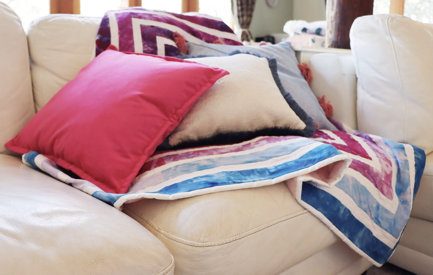 Colourful chenille cushion cover with cotton fringe and quilt on a beige sofa in a living room setting