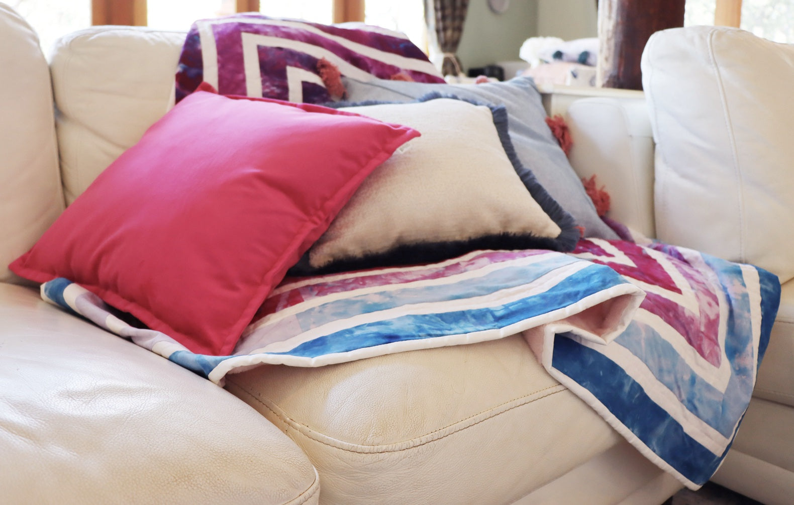Colourful chenille cushion cover with cotton fringe and quilt on a beige sofa in a living room setting