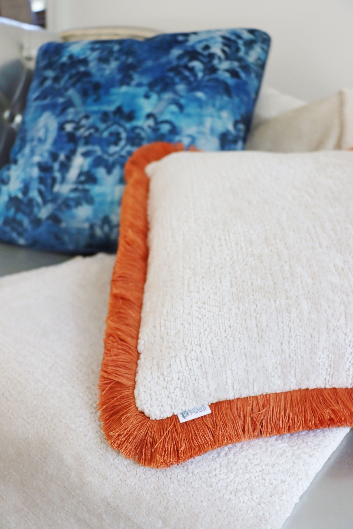 Close-up of a textured chenille cushion cover with cotton fringe on a couch.